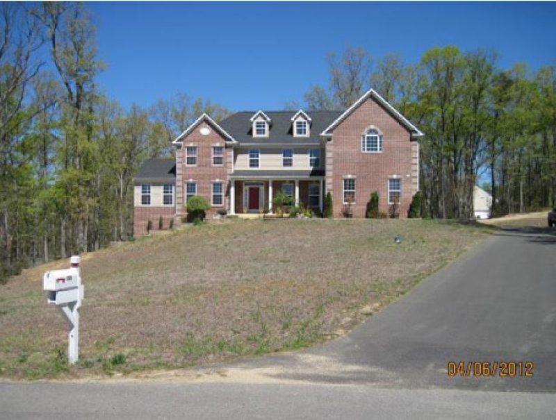A two-story brick house with a large, partially bare front yard, scheduled for new bermudagrass sod installation.
