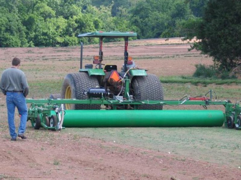 A worker observes a tractor outfitted with equipment for laying polypropylene netting, which strengthens the sod and improves harvest efficiency.