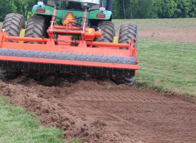 Soil preparation using a tractor-mounted tilling machine, a crucial step before sod installation.