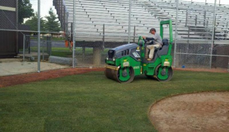 A roller is being used to achieve both sod-to-soil contact and to smooth the playing surface of this baseball field.