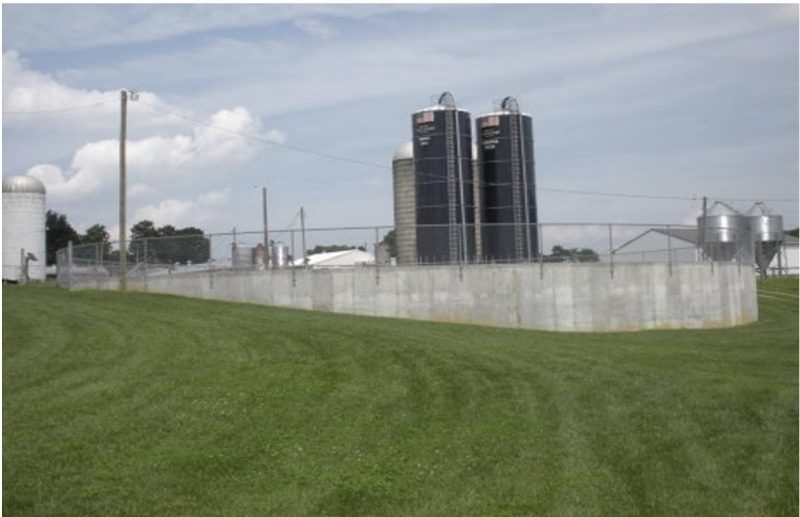 Dark grey storage structure surrounded by a fence and bright green grass