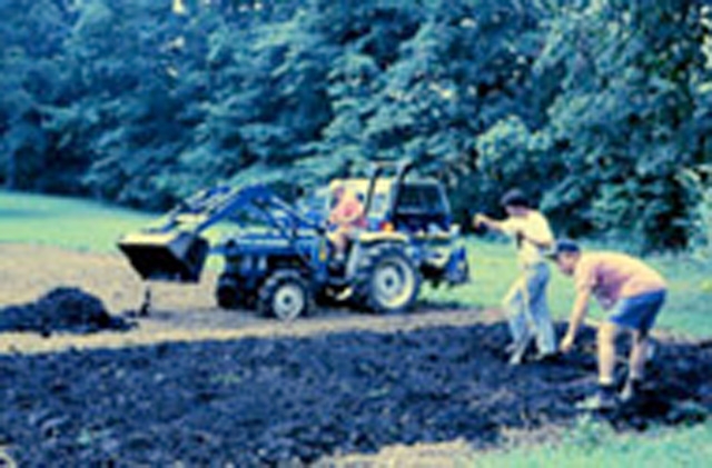 A picture of two people and an excavator working on compost