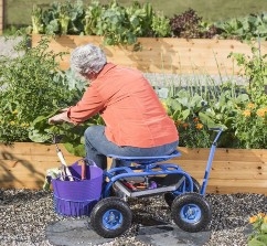 A person siting on a blue garden scooter. The scooter has four wheels and is equipped with a long handle and a basket.