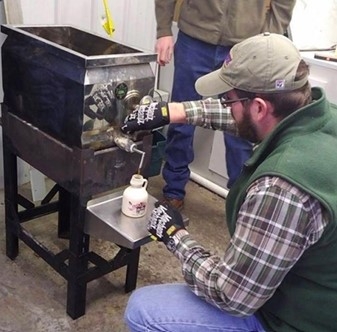 A man weraing gloves, bottling finished maple syrup for sale