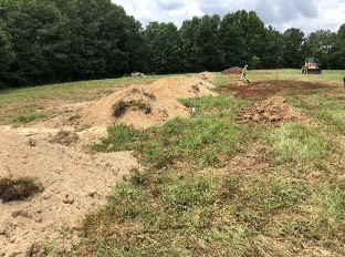 An Image multiple  above ground burial trenches fully covered with soil. The soil is a mound over the trench approximately two feet high in the center. 