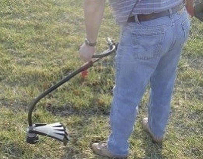 An image of a person from the waist down using a string hammer in a patch of green grass.