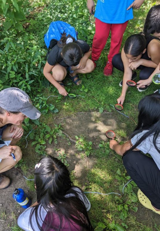 A group of youth crouch near the ground holding hand lenses.