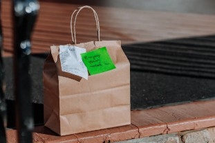 Sealed brown paper take out bag with staples on porch for contactless delivery.