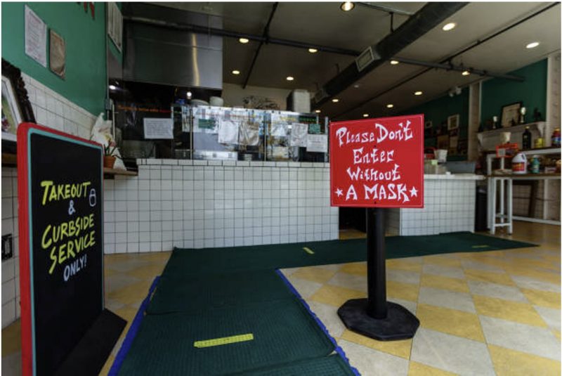 Inside view of restuarant. A restaurant adapts to Covid-19 with signs reading "Takeout & curbside service only" and "Please don't enter without a mask," and with yellow spacing markers on the floor for social distancing.