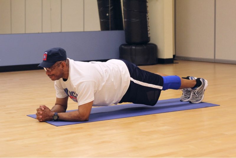 A man Lying on the ground with the elbows in line with the shoulder and the feet shoulder width apart. he is pushing his body up bearing the weight on the forearms and feet, Keeping his body straight.