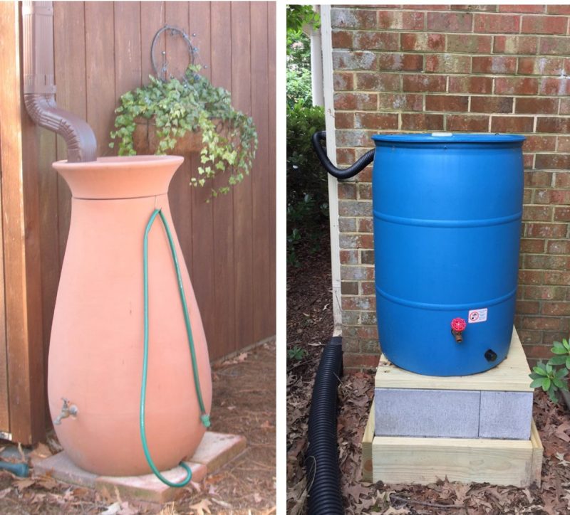 A tan rain barrel in front of a brown sided exterior wall on the left with a brown downspout feeding into its top, on the right is a blue rain barrel in front of a brick exterior wall and a black hose connecting the downspout to the top of the barrel.