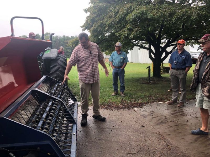 An Extension agent discusses an edamame pod harvester with onlookers.